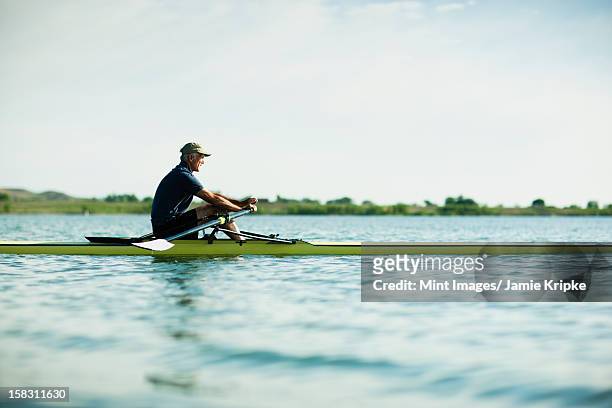a mature man in a rowing boat on the water. - single scull stockfoto's en -beelden