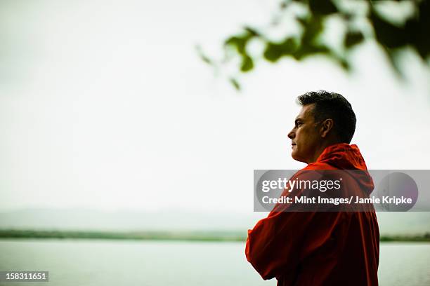 a middle aged man in a red jacket looking over water, deep in thought. - red coat stock pictures, royalty-free photos & images