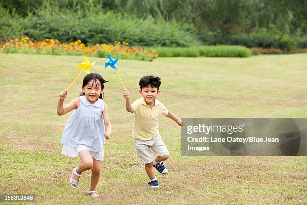 excited children playing paper windmill - windrad natur wiese stock-fotos und bilder