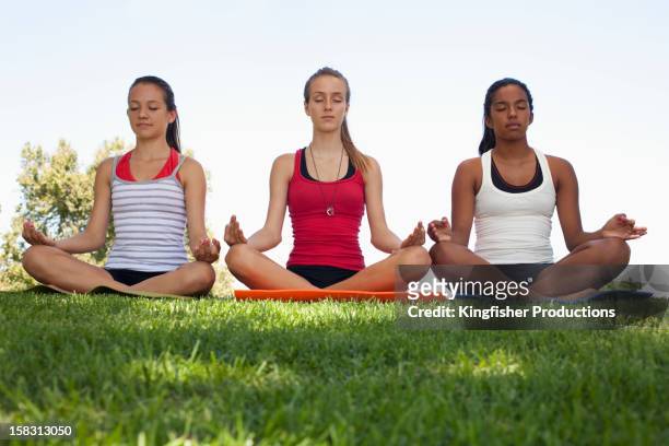 friends sitting in grass practicing yoga - yoga teen stock pictures, royalty-free photos & images