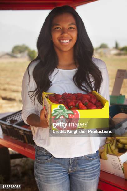 teenage mixed race girl holding strawberries at fruit stand - mixed farming stock-fotos und bilder