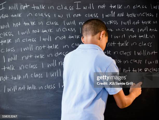 hispanic boy writing punishment on blackboard - school punishment stockfoto's en -beelden