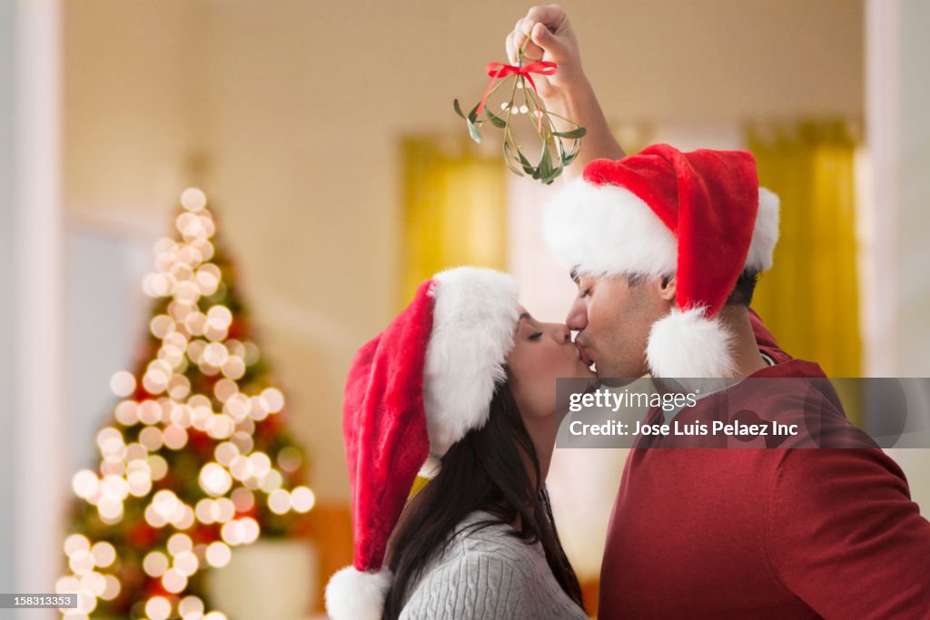 Couple in Santa hats kissing underneath mistletoe