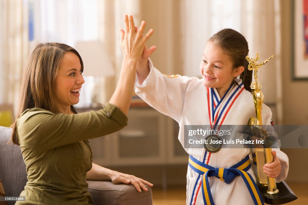 Caucasian mother high-fiving daughter for karate win