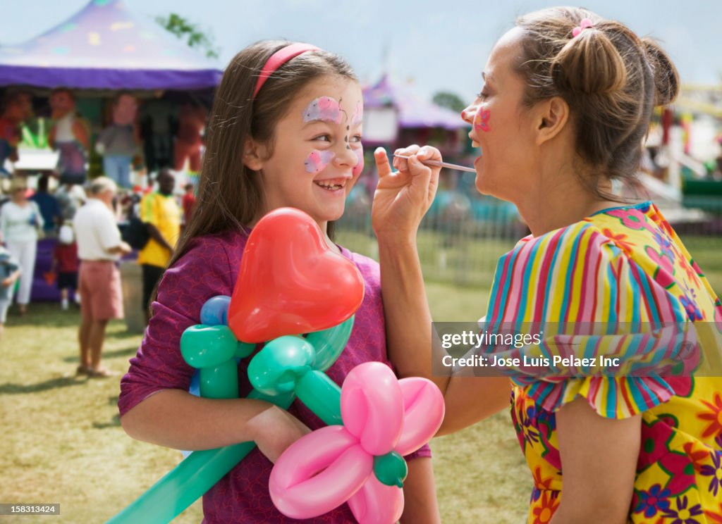 Caucasian girl having face painted at fair