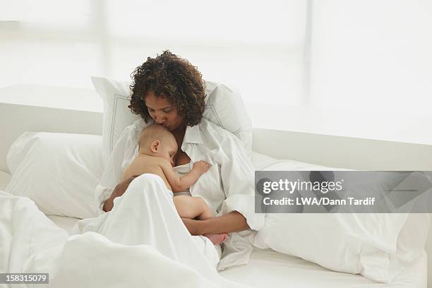 black mother laying in bed with baby - chest kissing stockfoto's en -beelden