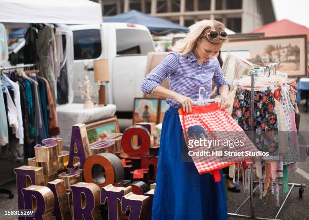 caucasian woman shopping for apron in flea market - vintage clothing stock pictures, royalty-free photos & images