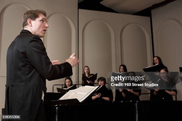 caucasian conductor leading choir on stage - coro foto e immagini stock