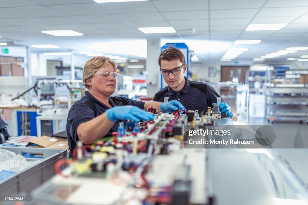 Engineer mentoring apprentice in medical electronics machinery manufacturing factory
