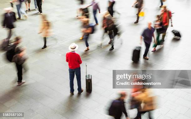 senior traveler surrounded by blurred motion of people at train station - top priority stock pictures, royalty-free photos & images