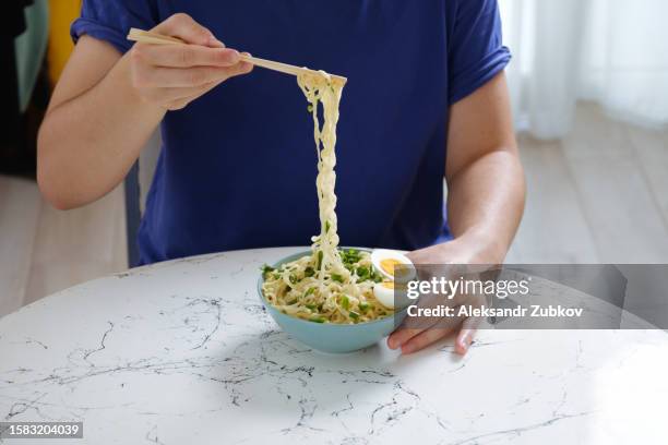 a man eats cooked instant noodles without meat, sprinkled with spices, herbs. a young man, a student, a teenager eats asian chicken noodle soup on the background of a dining kitchen table. a simple life. family life. prepare it yourself. - inexpensive fotografías e imágenes de stock