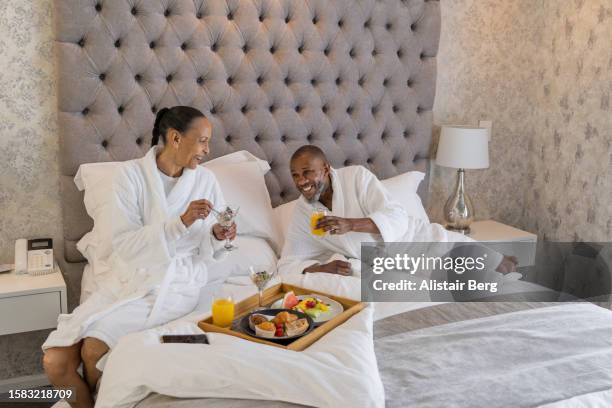mature couple enjoying breakfast in bed in a luxury hotel suite - black couple honeymoon fotografías e imágenes de stock
