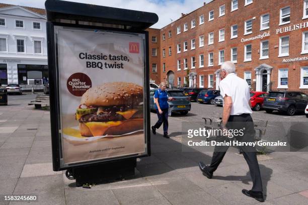 Members of the public pass a bus stop advertisement for McDonald's, the international fast food restaurant, and their new barbeque quarter pounder on...