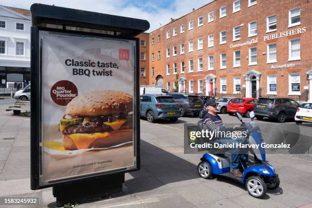 Members of the public pass a bus stop advertisement for McDonald's, the international fast food restaurant, and their new barbeque quarter pounder on...