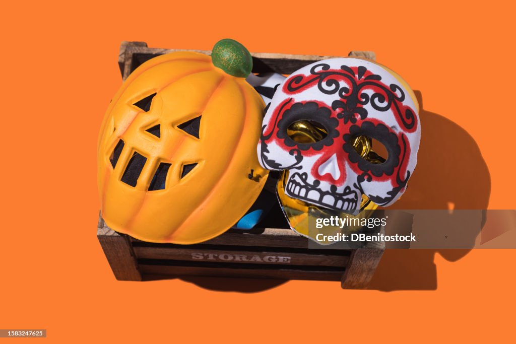 Wooden storage box with pumpkin and katrina Halloween masks typical of Mexico, on orange background. Halloween, day of the dead, celebration, costumes, spirits and festivity concept.