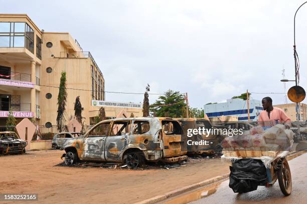 Street vendor pushes his cart past burned cars outside the headquarters of president Bazoum's Nigerien Party for Democracy and Socialism in Niamey on...