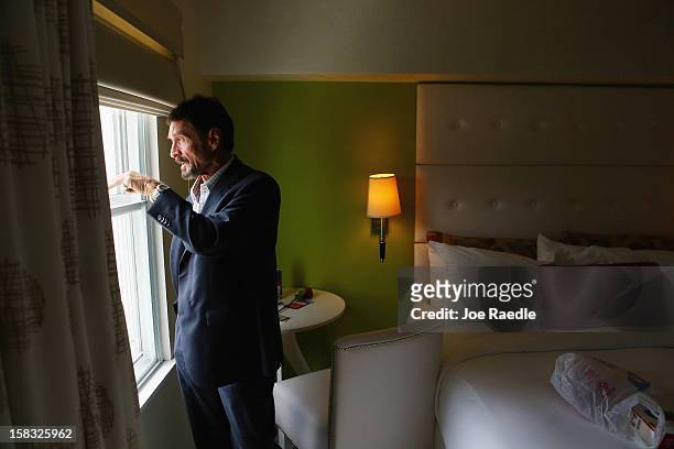 John McAfee looks out the window of his room at the Beacon Hotel where he is staying after arriving last night from Guatemala on December 13, 2012 in...