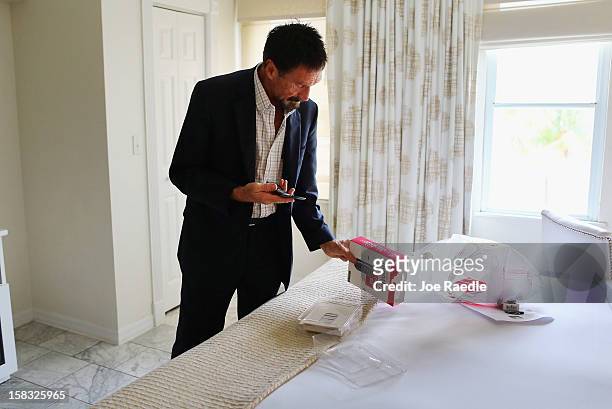 John McAfee unpacks a new cell phone in his room at the Beacon Hotel where he is staying after arriving last night from Guatemala on December 13,...