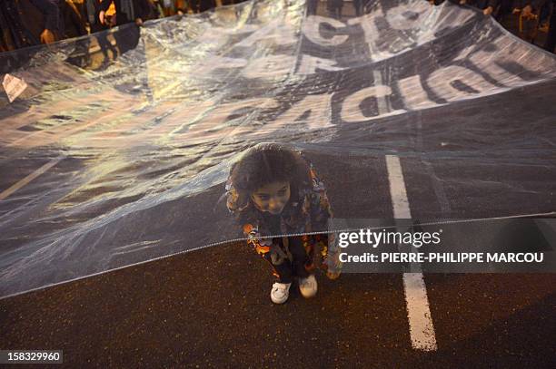 Young girl stands under a giant banner during a protest against government's austerity reforms and cuts in Madrid on December 13, 2012. Public...