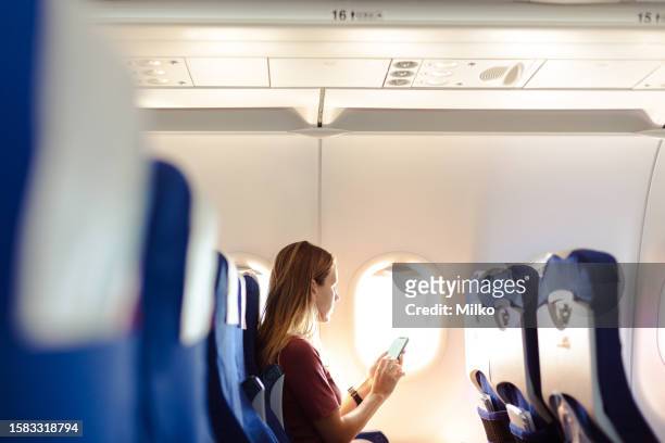 mujer en el avión sosteniendo un teléfono inteligente con pantalla blanca - aircraft wifi fotografías e imágenes de stock