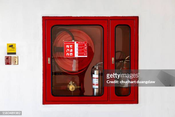 red fire hose cabinet and a fire extinguisher in the hotel corridor on white wall - brandslang stockfoto's en -beelden