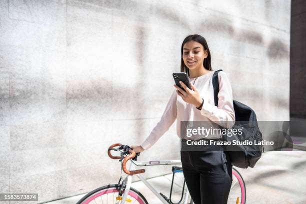 young woman using mobile phone while carry the bicycle in the city - student wellbeing stock pictures, royalty-free photos & images