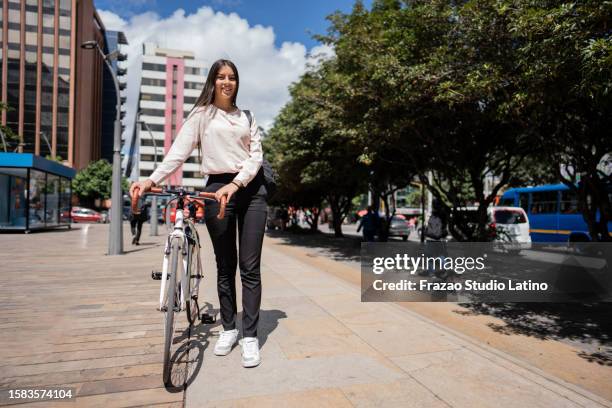 retrato de una mujer joven caminando mientras lleva la bicicleta en la ciudad - bogotá fotografías e imágenes de stock