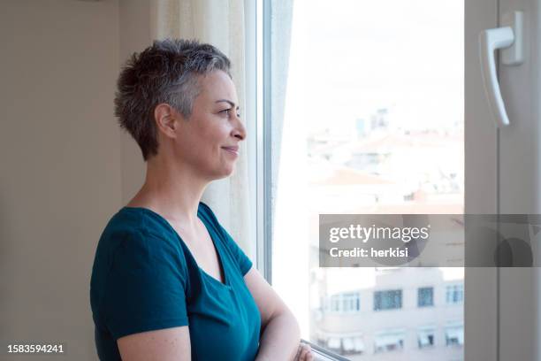 porträt der schönen reifen frau entspannen am fenster - einzelne frau über 40 stock-fotos und bilder