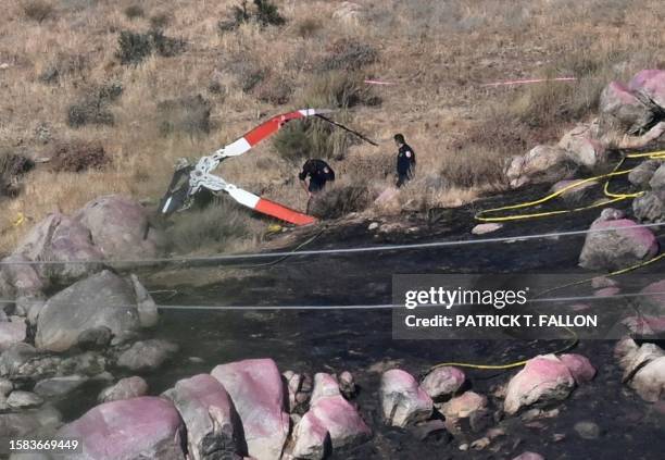 Investigators walk around rotor blades from one of the crashed helicopters on a burned hillside in Cabazon, California, on August 7, 2023. Three...