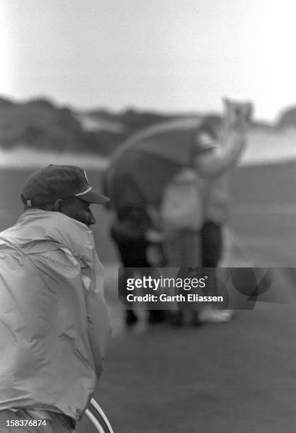 During the Bing Crosby National Pro-Amateur golf tournament, a caddie clutches a golf bag as golfers huddle against the wind on the 16th hole of the...