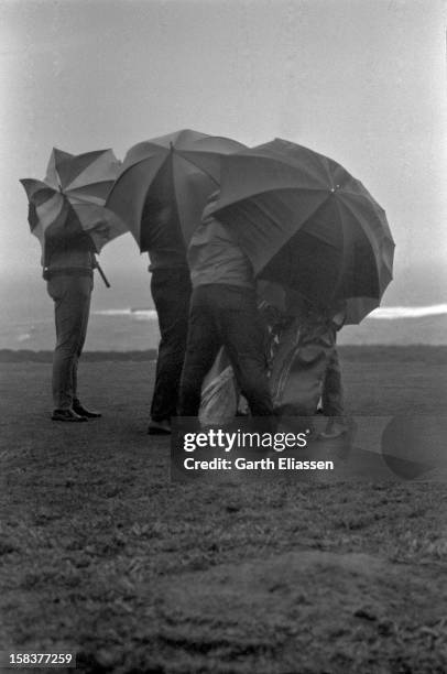 During the Bing Crosby National Pro-Amateur golf tournament, golfers huddle together against the wind and rain on the course near the 17th hole at...
