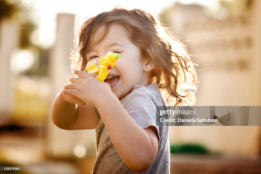 Boy with long, curly hair holding water gun