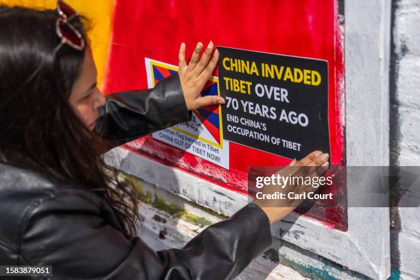 Woman sticks a Tibetan independence poster on an area of wall that had been graffitied with Chinese Communist Party ideology, on August 7, 2023 in...