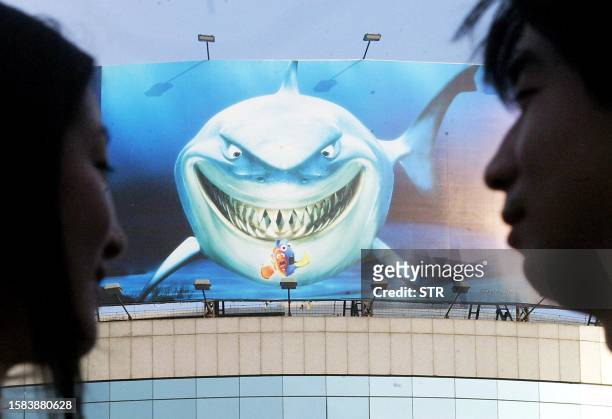 Chinese couple prepare to visit a new aquarium displaying a poster of hollywood film "Finding Nemo", in Beijing 29 July 2003. Tourism and travel to...