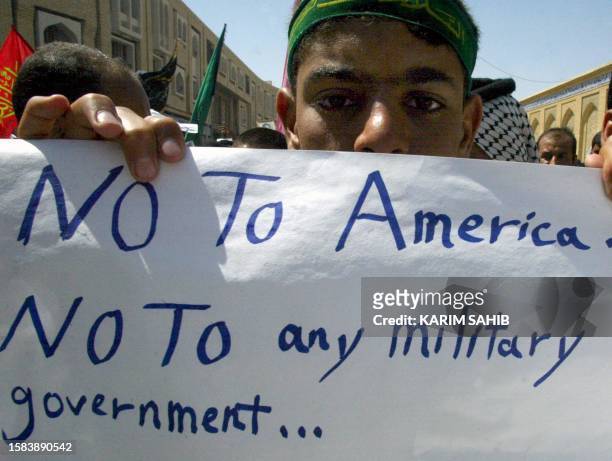 An Iraqi Shiite Muslim from a Hawza, a Shia religious school, displays an anti-American poster as several thousand Shiites chanted slogans 23 April,...