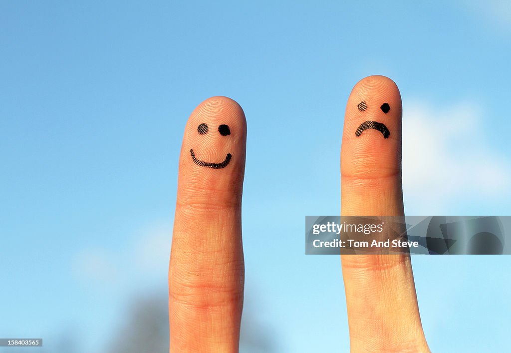 Happy and sad faces drawn on fingers