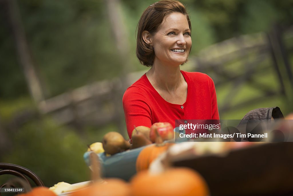  A woman in a red shirt, at a harvest table outdoors. 