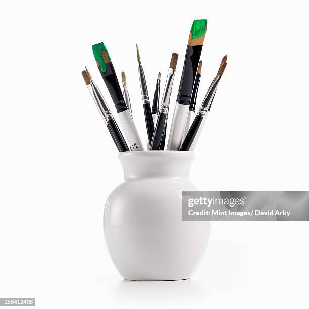 a white china pot full of paintbrushes, some still loaded with green paint. - art supplies fotografías e imágenes de stock