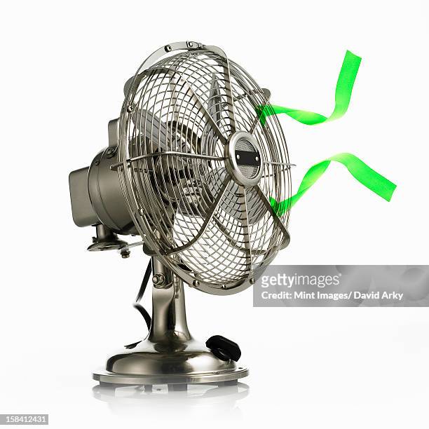 an electric fan with protective cage around the moving parts, and green streamers waving in the breeze. - electric fan stock pictures, royalty-free photos & images
