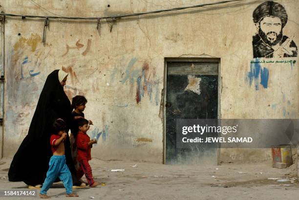 An Iraqi woman along with her children walks past a house adorned with a picture of rebel cleric Moqtada Sadr in the Sadr City neighborhood of...