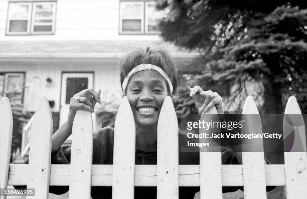American singer and actress Whitney Houston looks over the picket fence of her mother's home, West Orange, New Jersey, May 28, 1985.