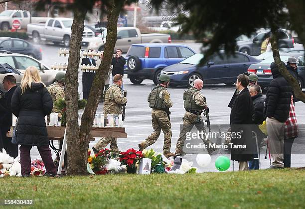 Connecticut State Police officers walk past a makeshift memorial to shooting victims while searching outside St. Rose of Lima Roman Catholic Church...