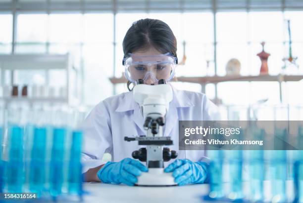 laboratory technician looking through microscope while examining genomic sample during research in laboratory - artigos-de-vidro-de-laboratório - fotografias e filmes do acervo