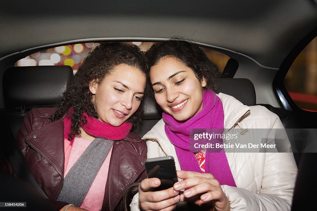 Women looking at phone in back of taxi.