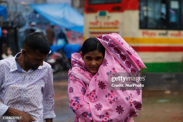 Woman holds her child as she crosses the road during rainfall in Dhaka, Bangladesh on August 8, 2023.