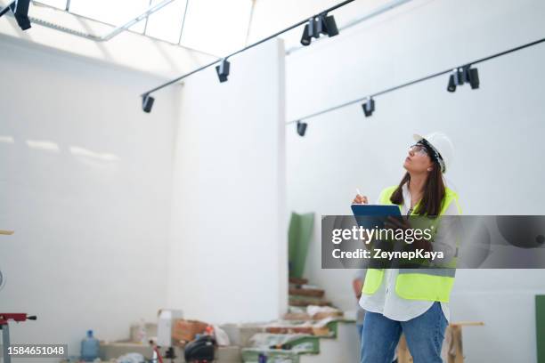 mujer con casco blanco protector, usando una tableta digital en el sitio de construcción - inspector fotografías e imágenes de stock