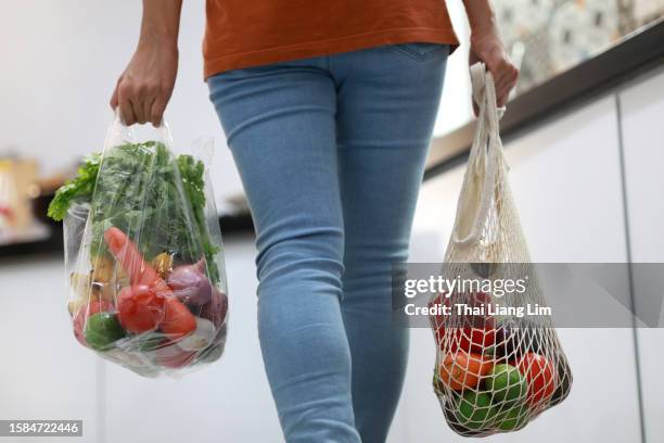 cropped image of an asian woman holding mesh eco bag shopper and plastic shopping bags in the kitchen - plastic bag stock pictures, royalty-free photos & images