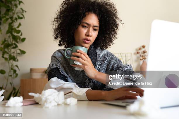 sick african american woman working from home office using laptop drinking hot beverage covered with blanket. - hot latina women 個照片及圖片檔