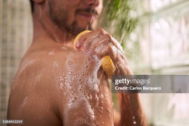 unrecognizable man taking a shower, using sponge to rub his shoulder. - douche photos et images de collection