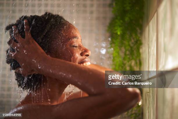 cheerful young african woman taking a refreshing shower at home, washing her hair. - woman washing face stockfoto's en -beelden